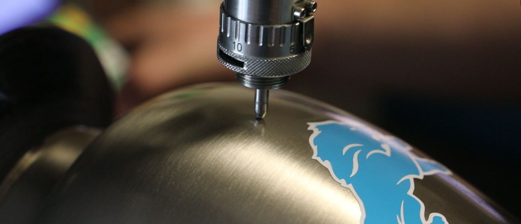 Engraving a metal cremation urn that features a Detroit Lions logo.