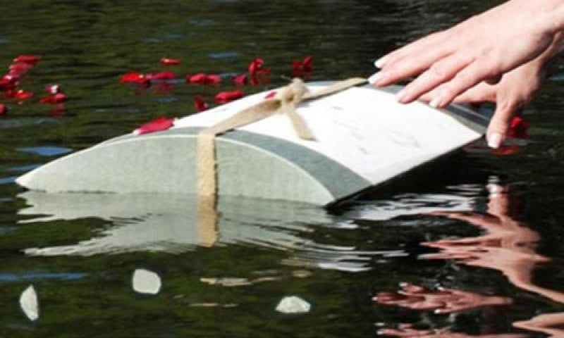 Biodegradable burial urn being released on the water with rose petals.