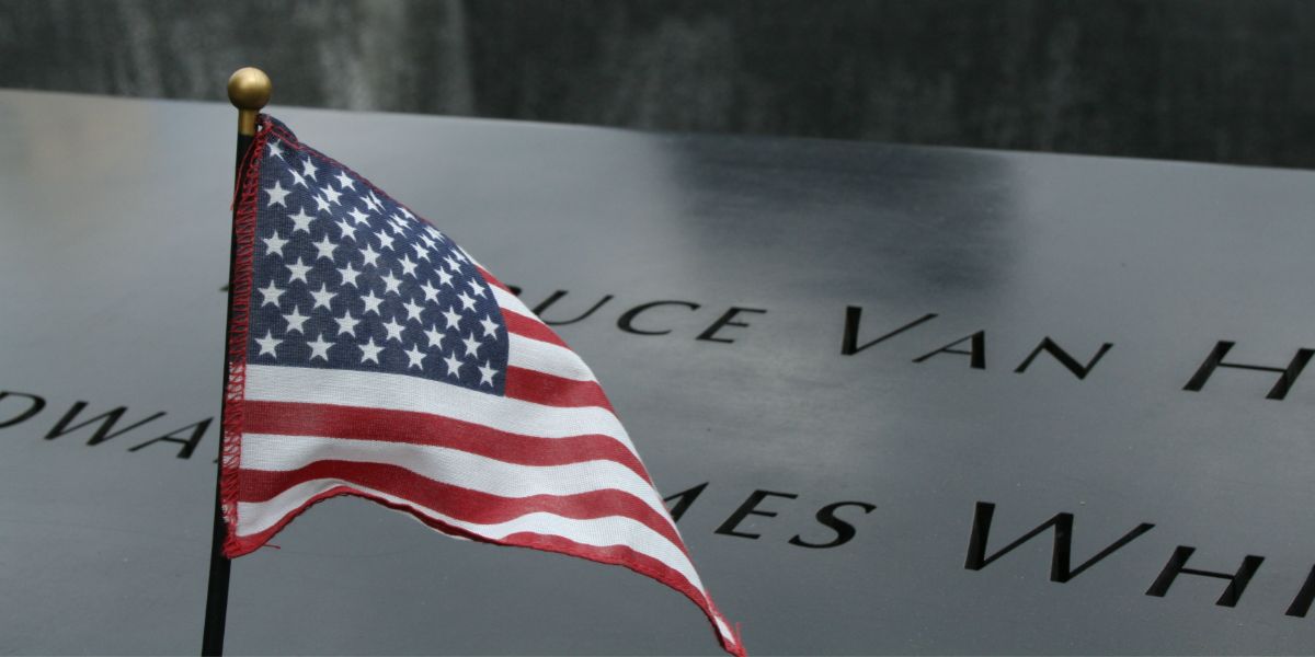Small American flag in front of marble memorial.