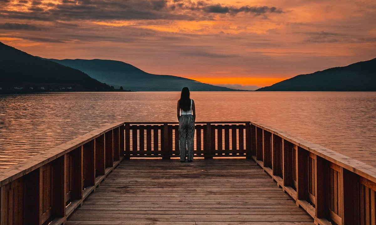 Woman standing at the end of a dock overlooking the sunset.
